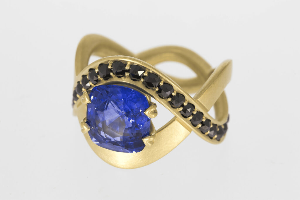 verspielter Goldring mit blauem Edelstein und kleinen schwarzen Edelsteinen